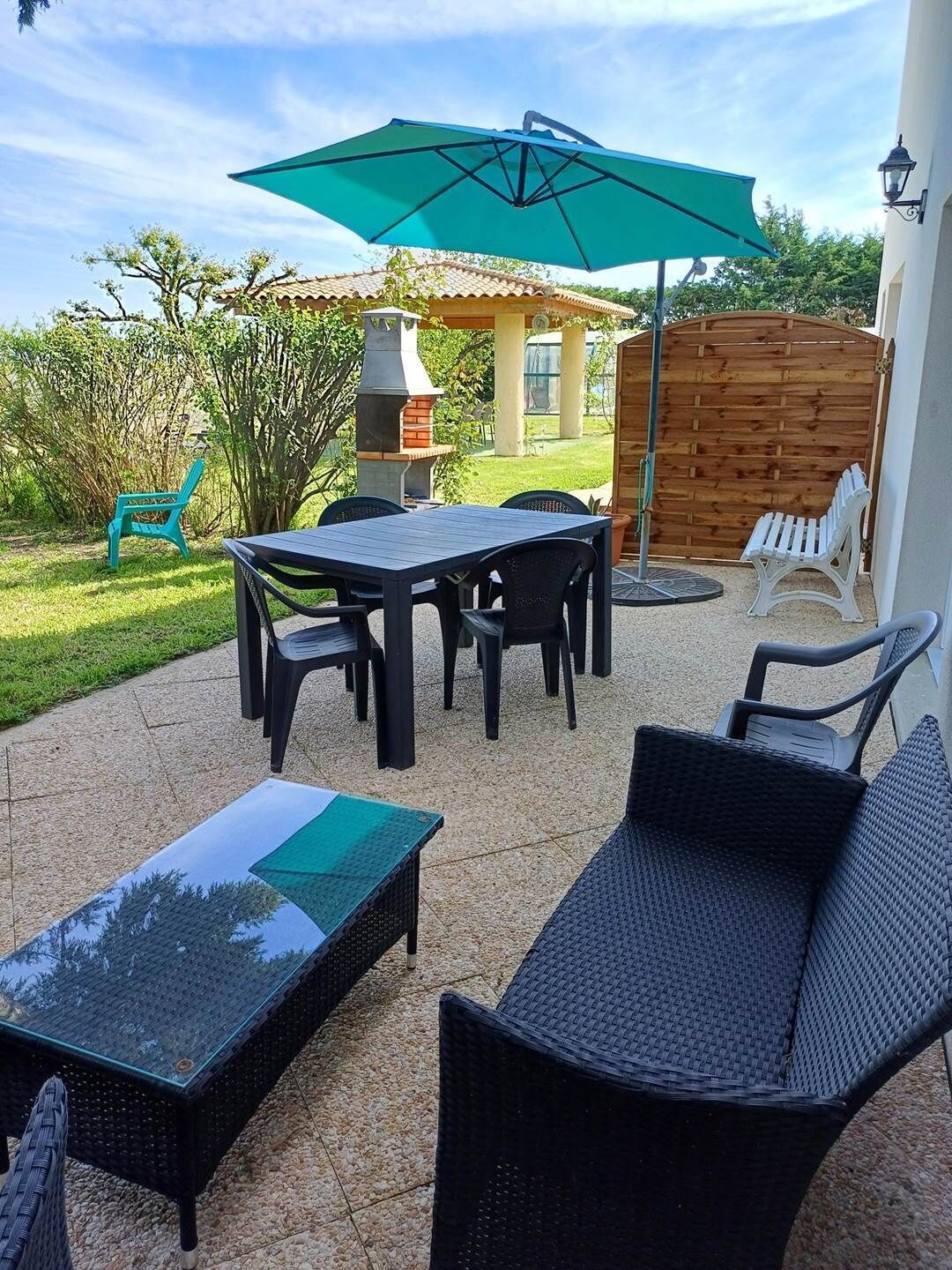 Un patio al aire libre con una mesa, sillas, una sombrilla verde y una parrilla.