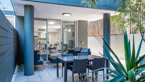 A modern outdoor patio with a dining area, including a table and chairs, and a view into the adjacent kitchen. - City Edge Albion Pool, Patio & City Access (Albion)