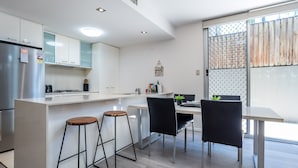 A modern kitchen with a dining area, featuring a stainless steel refrigerator, white cabinets, a black countertop, and a dining table with two chairs. - City Edge Albion Pool, Patio & City Access (Albion)