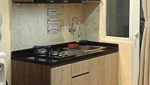 Kompakti keittiö, jossa on puukaapit, kaasuliesi, pesuallas ja ikkuna, jossa on verhot.