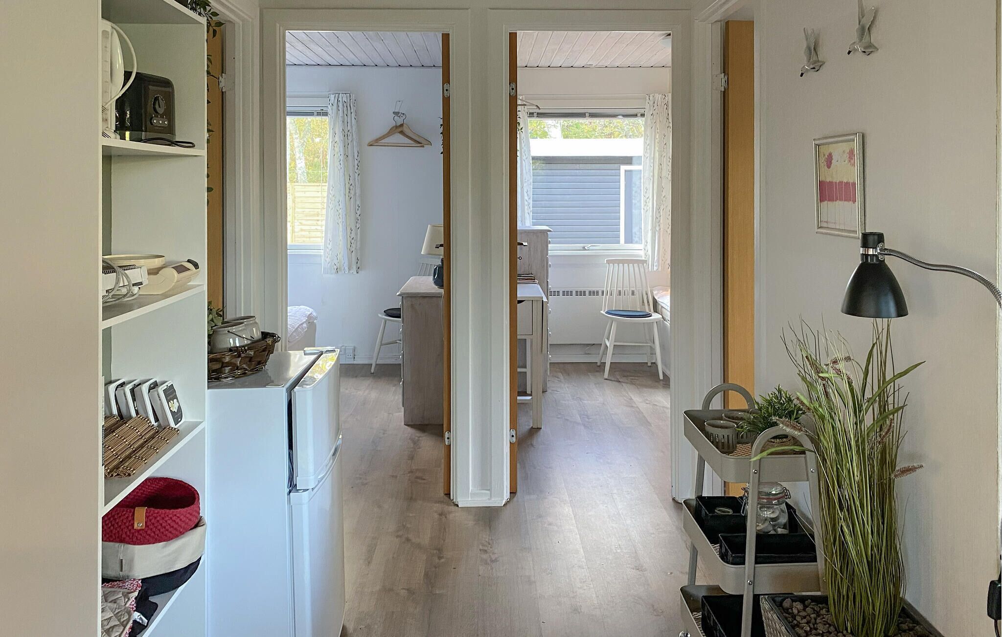 A narrow hallway with a white refrigerator, a small table with a chair, and a hanging coat rack.