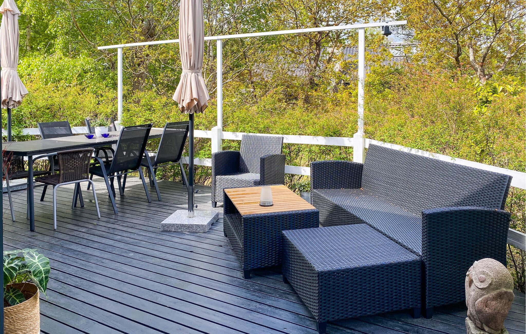 An outdoor deck with a table and chairs, a sofa, and a pergola with umbrellas.