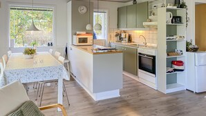 A modern kitchen with white cabinets, a microwave, oven, and a sink. There is a dining area with a table and chairs. - Amazing home in Glesborg with WiFi (Glesborg)