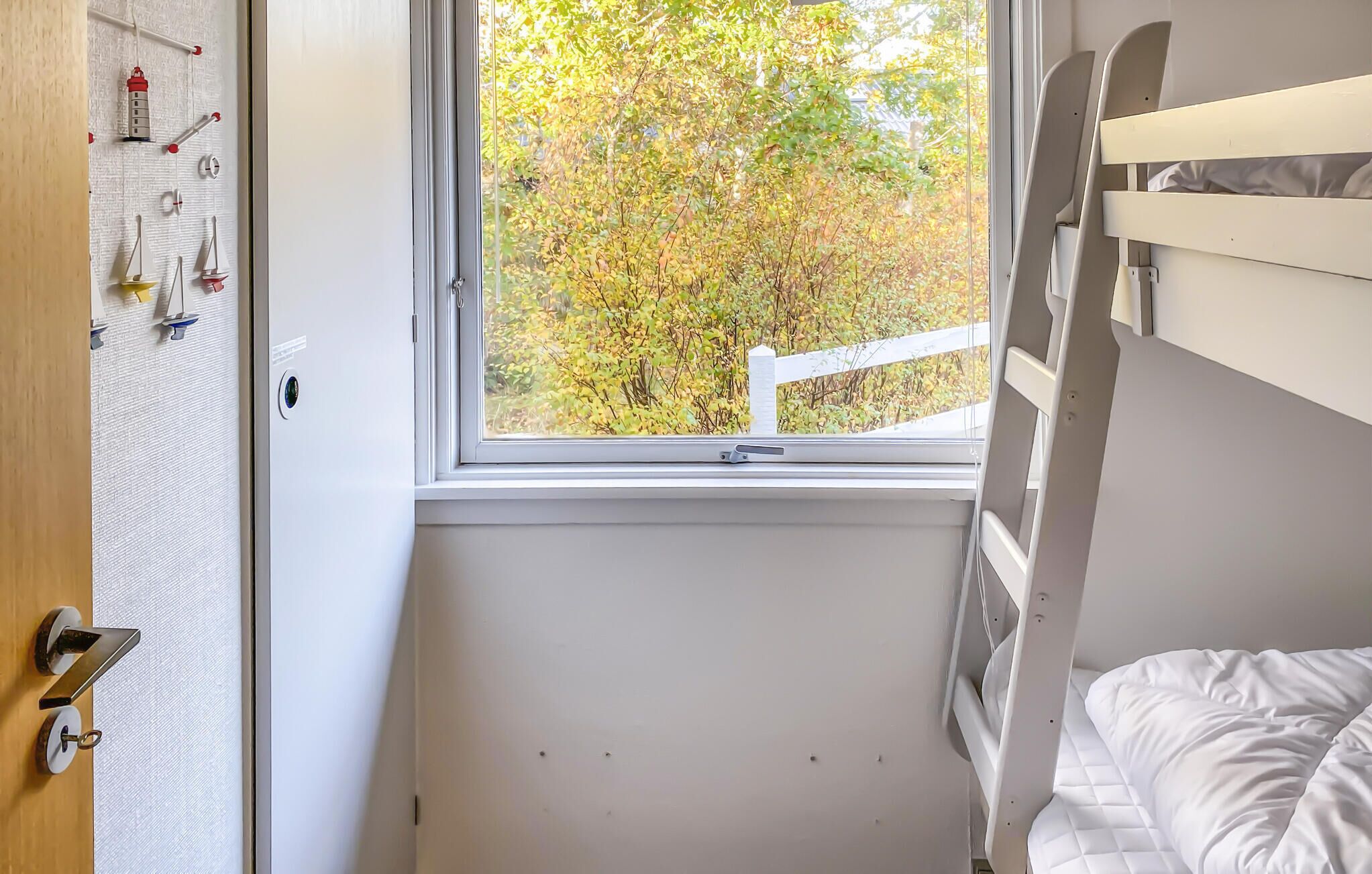 Una camera da letto con un letto a castello, una finestra vista alberi e un attaccapanni a muro con diversi oggetti.