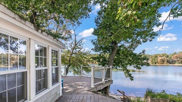 A lakeside cabin with a wooden deck, large windows, and a view of the lake.