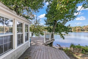 Un chalet au bord du lac, doté d’une terrasse en bois, de grandes fenêtres et offrant une vue sur le lac.