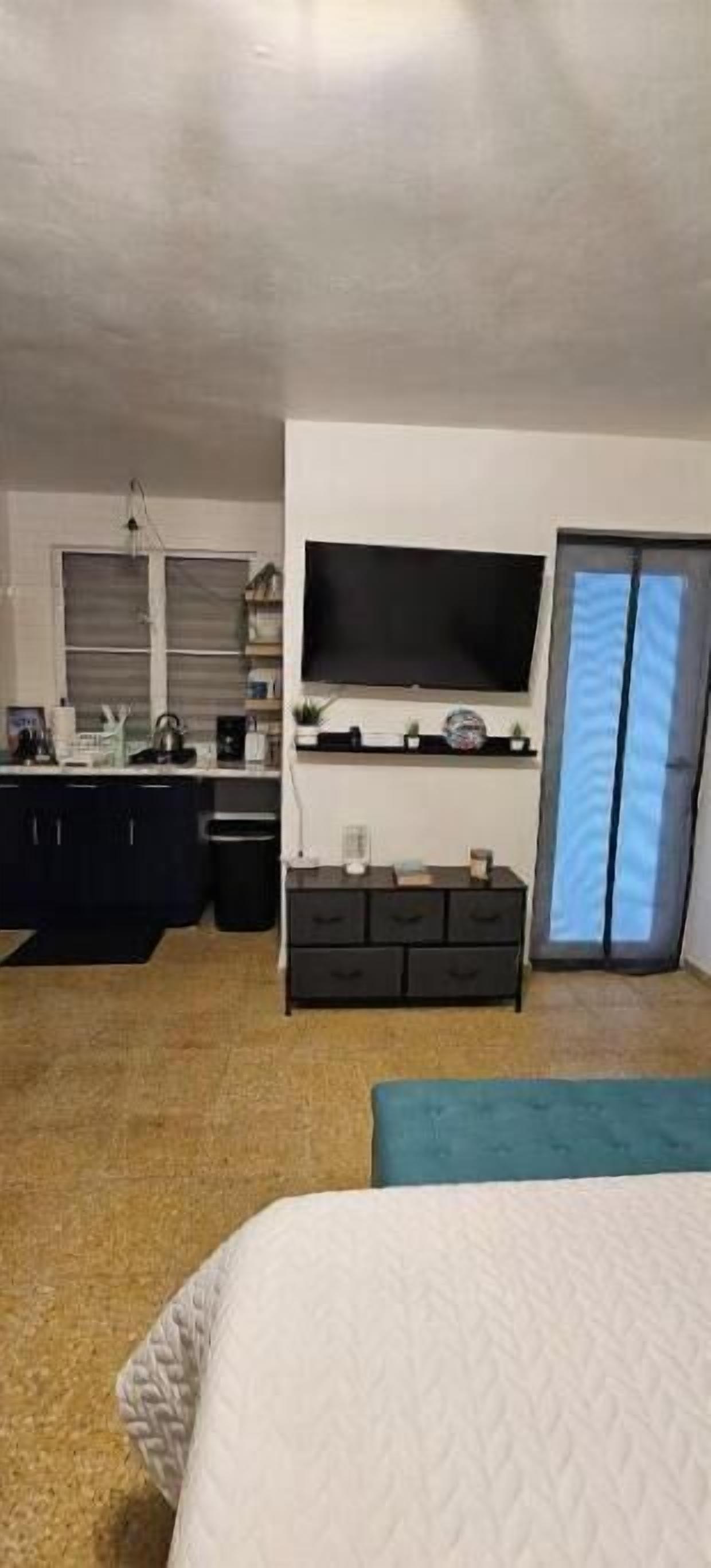 A bedroom with a bed, a dresser, a television mounted on the wall, and a window with curtains.