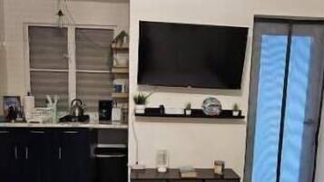A bedroom with a bed, a dresser, a television mounted on the wall, and a window with curtains.