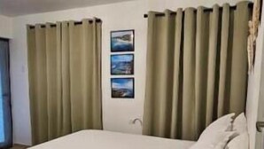 A hotel room with a bed, curtains, a wall-mounted artwork, and a carpeted floor. - Studio Apt in Añasco beach 15min drive to Rincon (Añasco)