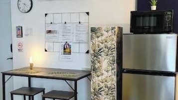 Een compacte keuken met een koelkast, een magnetron en een kleine eethoek met krukjes.