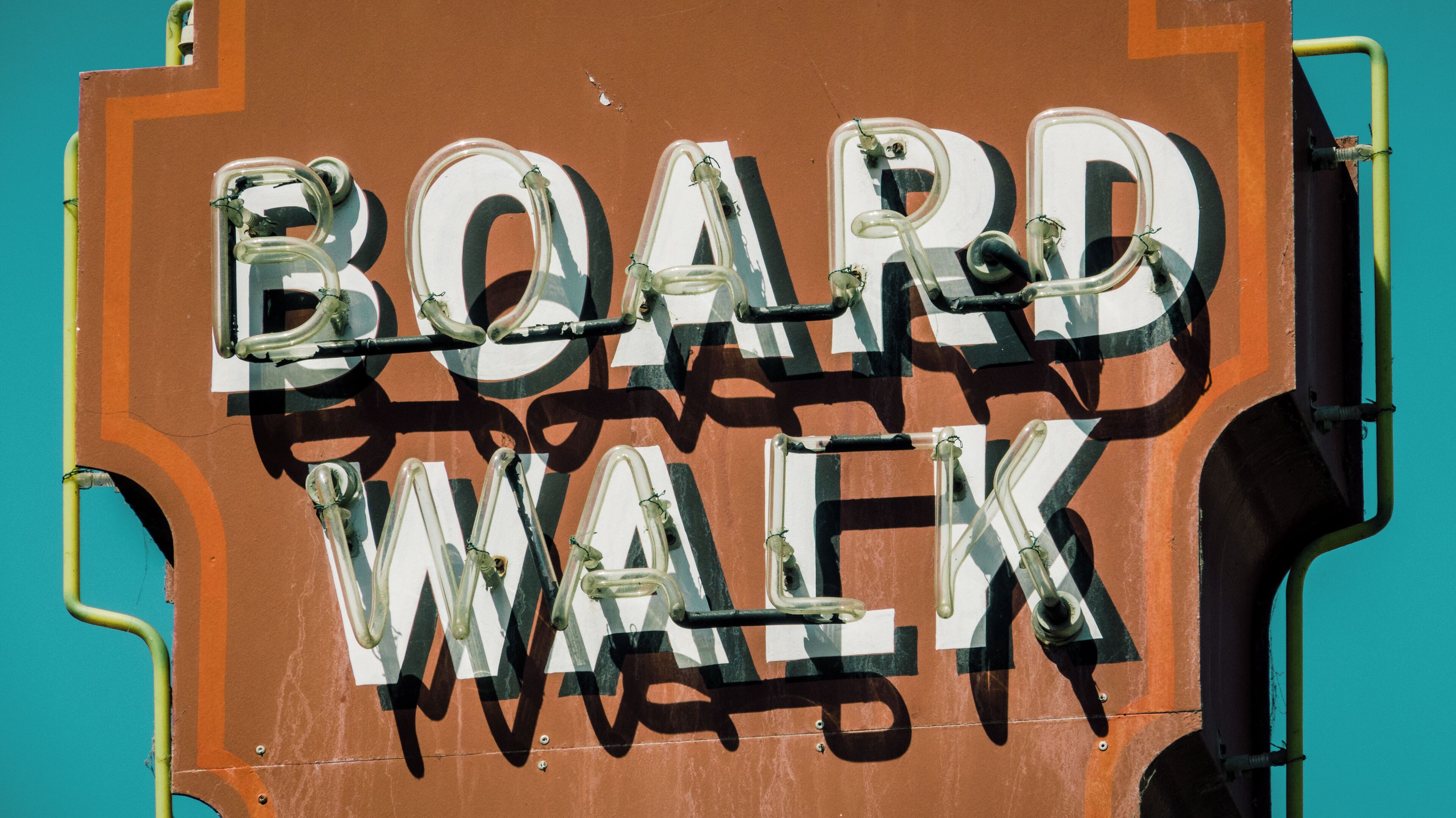 A sign with the words "BOARD WALK" in a stylized font, mounted on a brown structure with a turquoise background.