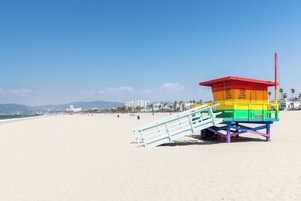 A lifeguard tower with a red top and a multi-colored body on a beach.