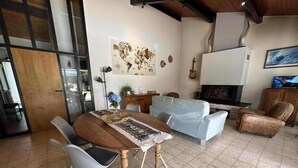 A living room with a wooden dining table, two white chairs, a light blue sofa, and a fireplace.