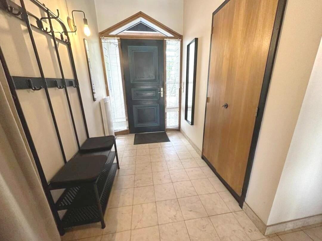 A hallway with a wooden door, a bench, and wall-mounted hooks.