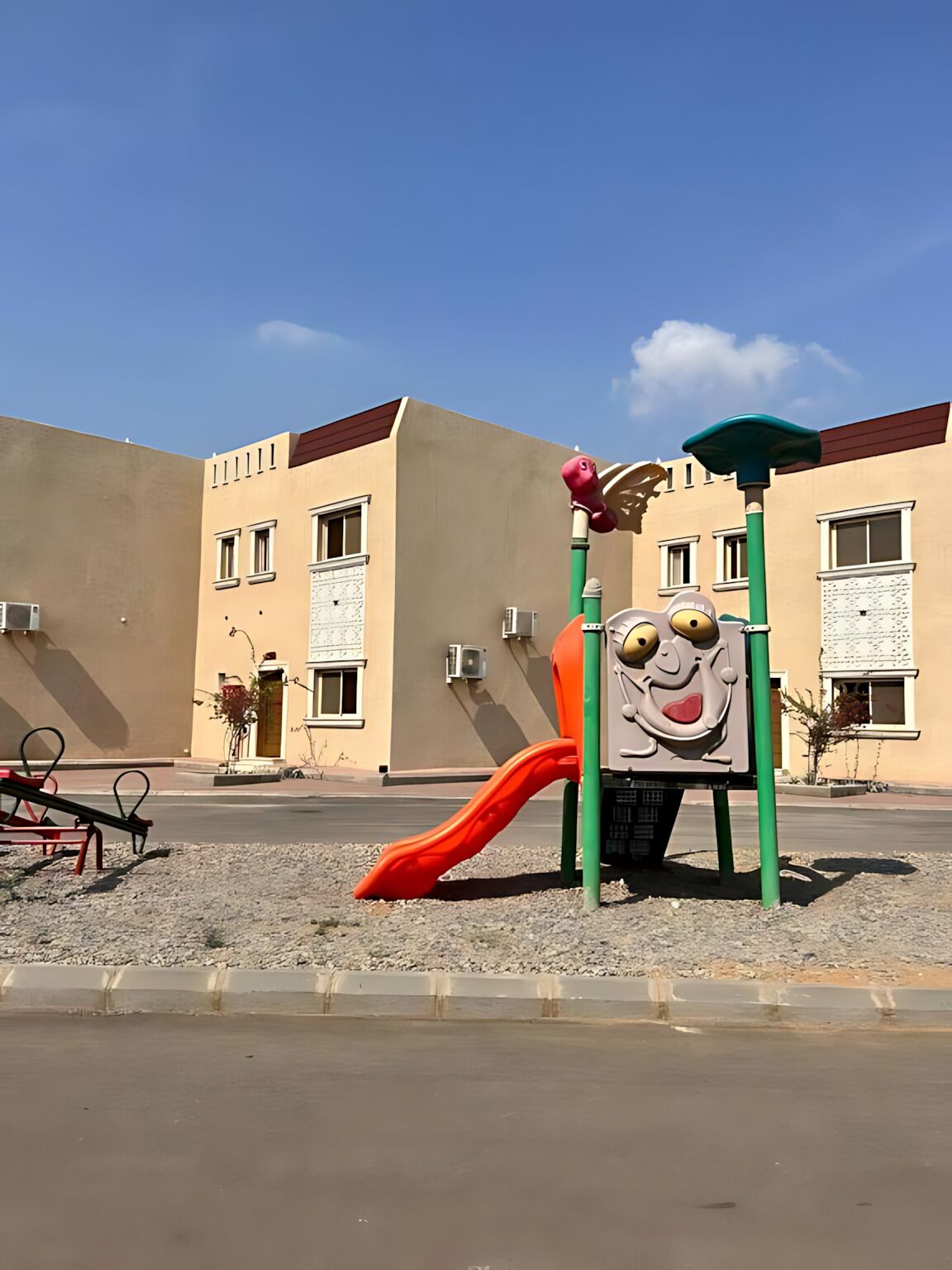 Un parque infantil con tobogán y estructuras para escalar frente a un edificio con varias ventanas y unidades de aire acondicionado.