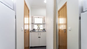 Ein schmaler Korridor mit weißen Wänden, Holztüren und einem Fenster mit Pflanze.