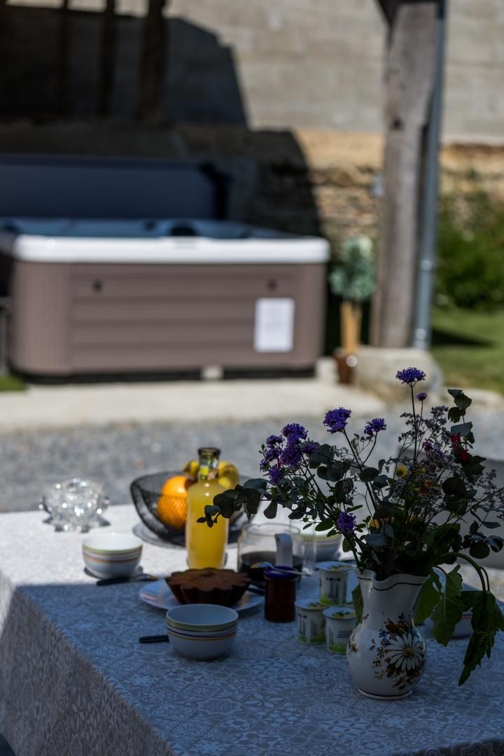 A table with a hot tub in the background, a vase with flowers, and various items on the table.