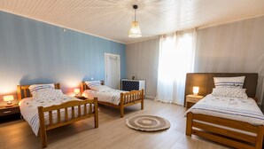 Quarto com três camas de madeira, um ventilador de teto e um tapete redondo pequeno.