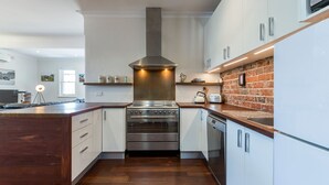 A modern kitchen with a central island, stainless steel appliances, and a brick accent wall. - UrbanStyle Claremont Apartment (Mount Claremont)