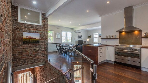 A spacious kitchen with modern appliances, a brick accent wall, and a dining area with a glass railing. - UrbanStyle Claremont Apartment (Mount Claremont)