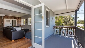 A modern living room with a sofa, a dining area with stools, and a balcony with a view of the street. - UrbanStyle Claremont Apartment (Mount Claremont)