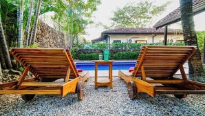 Two wooden lounge chairs facing a small pool with a table in between, surrounded by pebbles and greenery. - Casa Tropical - Fully equipped house with private pool and BBQ (Villareal Tamarindo)