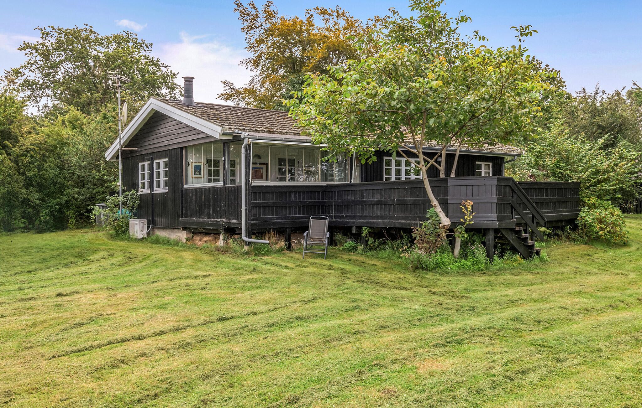 A two-story wooden house with a balcony, surrounded by a grassy field and trees.