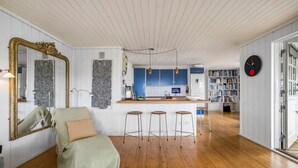 Un vaste espace de vie doté d’un plancher en bois, d’un grand miroir, d’un fauteuil vert et d’un coin bar avec des tabourets.