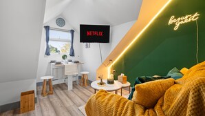 A modern room with a cozy yellow sofa, a flat-screen TV, and a neon sign.