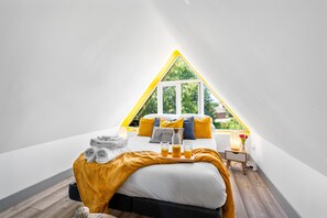 A triangular attic bedroom with a bed, pillows, a tray with glasses and orange juice, and a window with a view of greenery. - Cozy 2-Bed Attic | 5 Mins to BHX Airport & NEC (Marston Green)