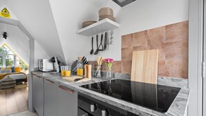 A modern kitchen with grey cabinets, a black stove, and a marble countertop. There are utensils hanging on the wall and a wooden cutting board on the counter.