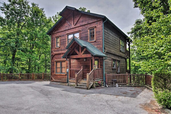 A two-story log cabin with a porch and a fenced driveway.