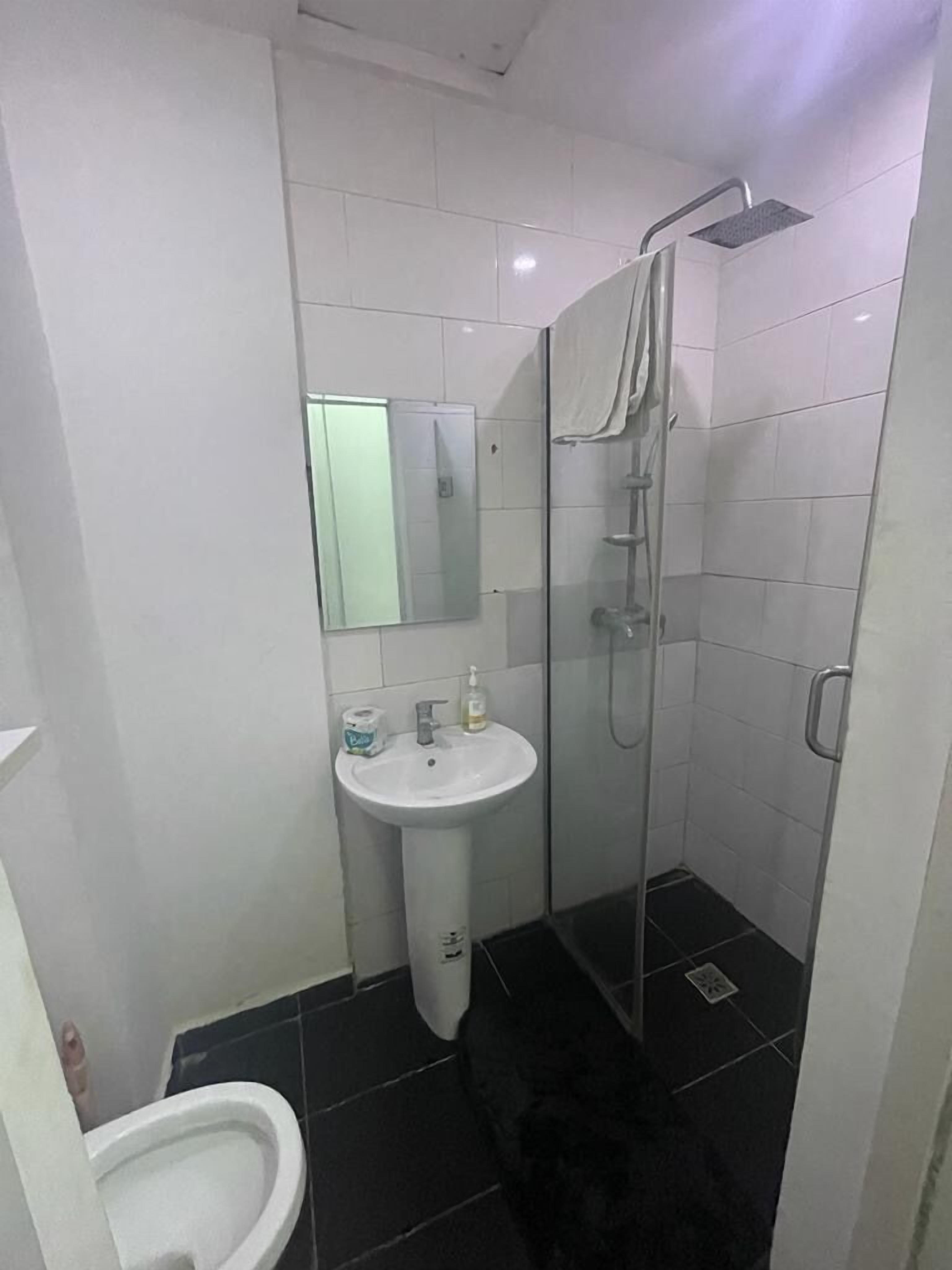 Un baño pequeño y funcional con un lavamanos blanco, un espejo, un inodoro y una zona de ducha con mampara de vidrio.