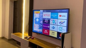 Een moderne woonkamer met een groot televisiescherm, bevestigd aan een houten console, waarop verschillende streamingdiensten worden getoond.