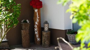 Et træskilt med teksten "WILLKOMEN", en rød blomst, en lygte og to fletkurve på en stenhylde.