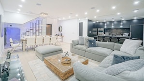 A modern living room with a grey sofa, a glass coffee table, and a dining area with a white table and chairs. - Luxury Heated Pool + BBQ + 15 Min To Beach (Miami)