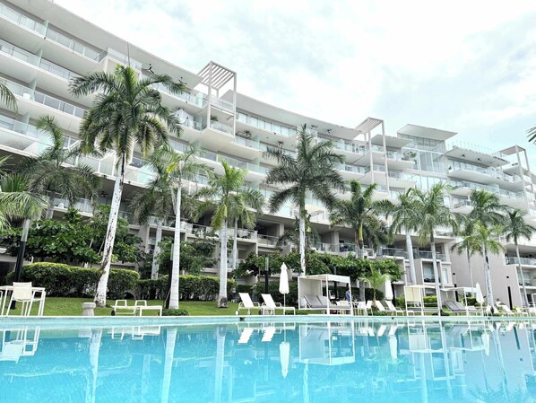Un hotel moderno con varios balcones, piscina y palmeras.