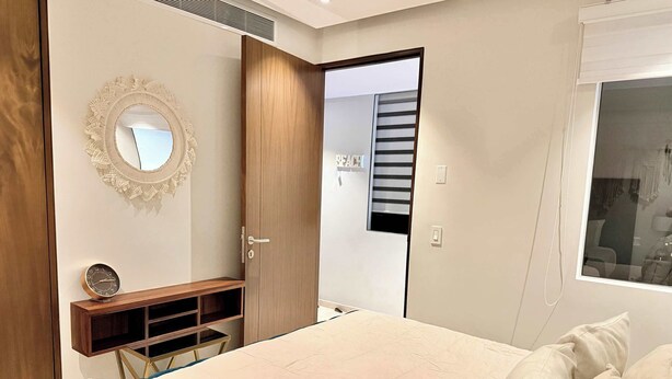 A bedroom with a bed, a wooden wardrobe, a mirror, a small table, and a window. - Bolongo: Your Exclusive Oceanfront Escape (Sayulita)