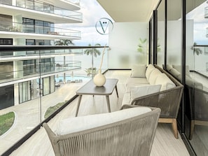 A modern balcony with a sofa, a table, and a view of a pool and building. - Tizate 3BR Private Beach Stunning View (La Cruz de Huanacaxtle)