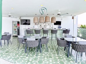 Un espacio moderno para comer al aire libre con barra, sillas de mimbre y piso estampado.