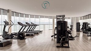 Une salle de sport moderne équipée de tapis de course, d’appareils de musculation et dotée d’une grande fenêtre offrant une vue sur la ville.