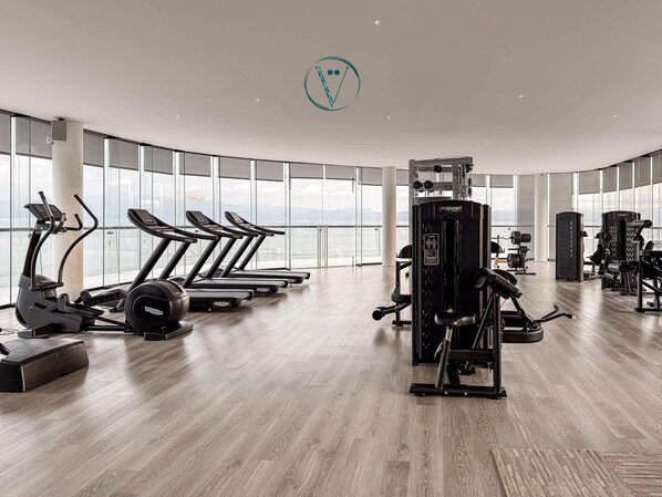 Un gimnasio moderno con cintas de correr, máquinas de pesas y un amplio ventanal con vistas a la ciudad.