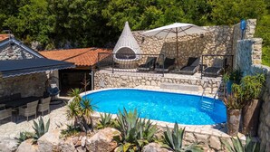 A stone pool with lounge chairs, a stone wall, and a conical structure.