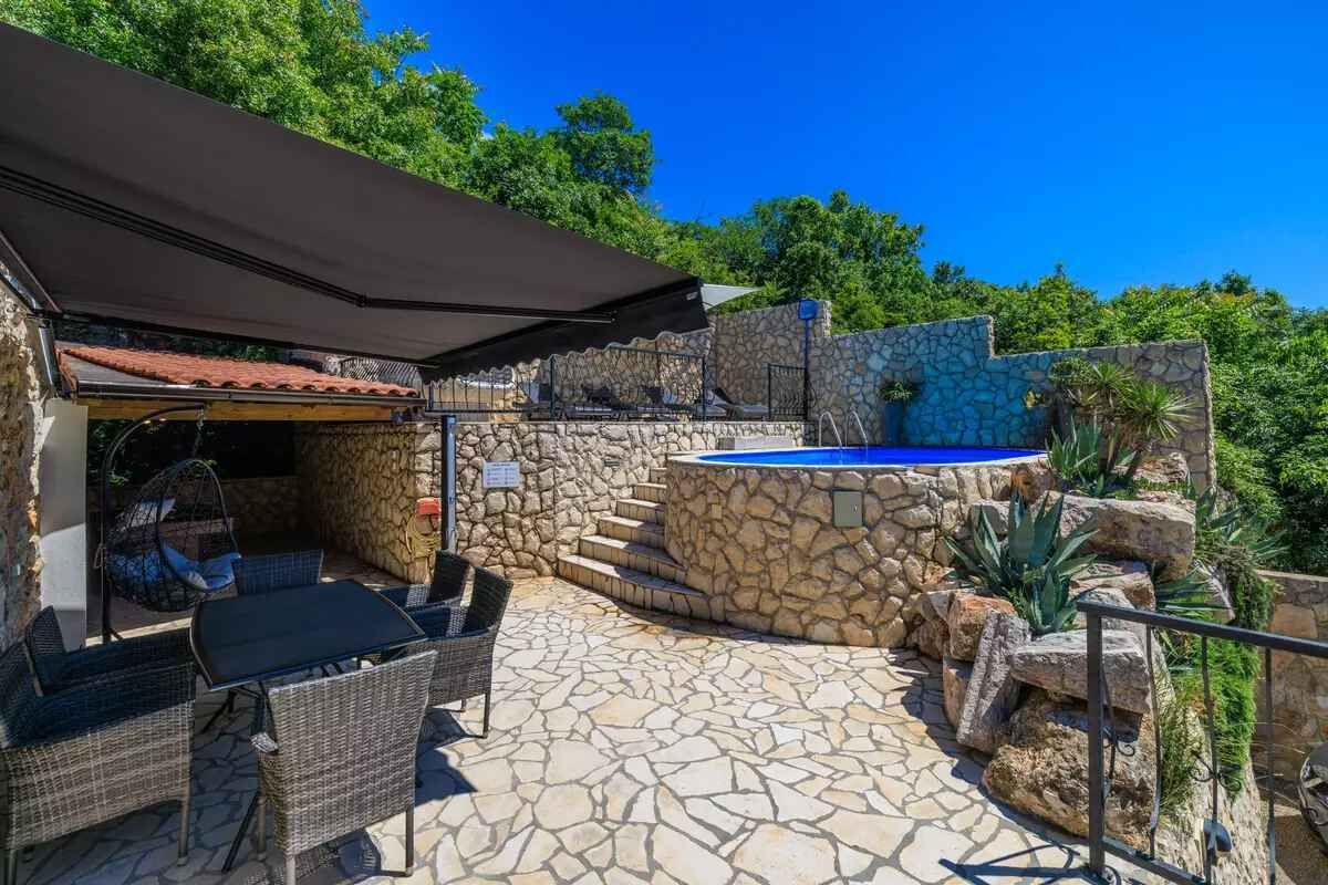 A stone patio with outdoor furniture, a swimming pool, and a covered seating area.