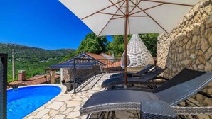 A poolside area with lounge chairs, a pergola, and a stone wall.