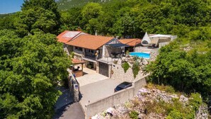 A hillside villa with a swimming pool, stone walls, and a red-tiled roof.