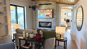 Un salon moderne doté d’une cheminée en pierre, d’un téléviseur à écran plat et d’un coin salon confortable avec un canapé et une table basse.