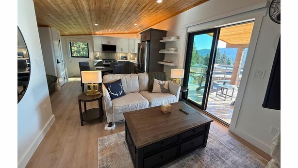 Un salon moderne avec un plafond en bois, un canapé, une table basse et une cuisine en arrière-plan.
