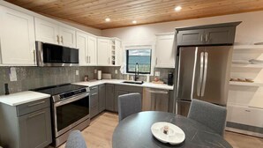 Une cuisine moderne avec des meubles blancs, des appareils en acier inoxydable et une table à manger ronde entourée de chaises grises.