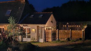 Un bâtiment rustique avec un toit en pente, un petit porche décoré de guirlandes lumineuses et un portail en bois.